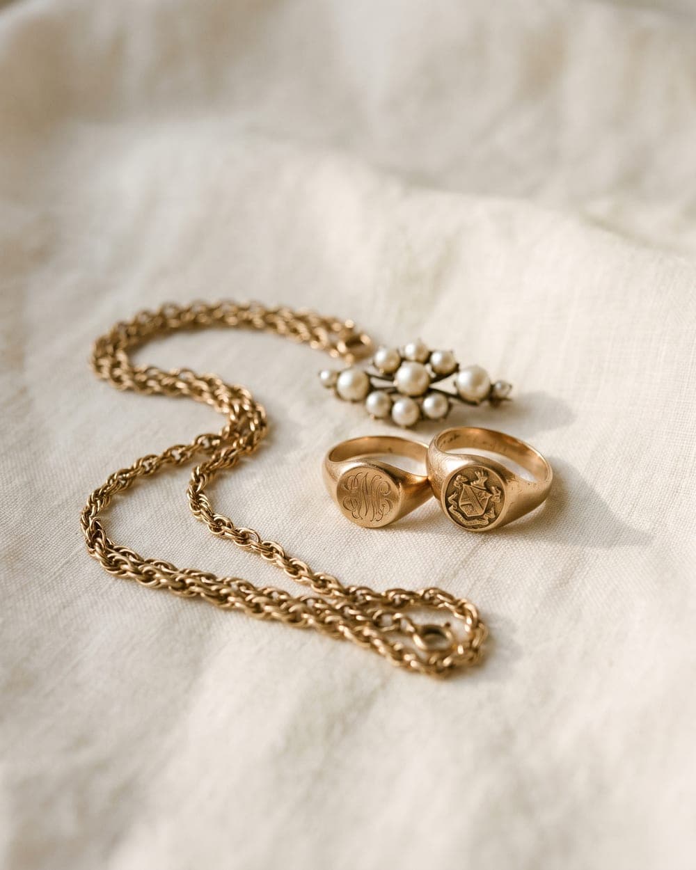 Erbschmuck auf Leinentuch: Goldkette, zwei Siegelringe und Perlenbrosche